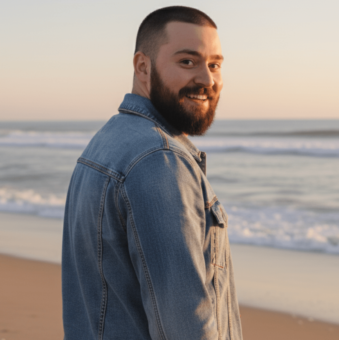 person wearing a stonewashed denim jacket on the beach at sunset, showing jacket fit and back panel design