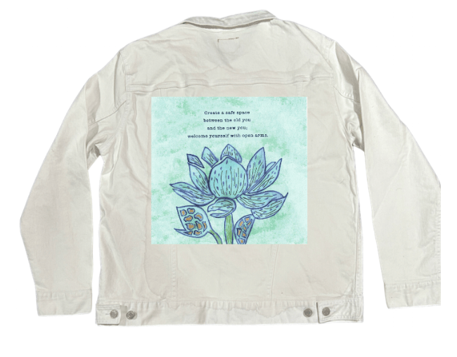 back view of a white denim jacket featuring the artwork “Always Welcome Yourself” by Canvas & Quotations, showing a blue lotus flower and inspirational quote on a light-green textured background. the artwork is digitally printed on the jacket’s back panel by DenimINK