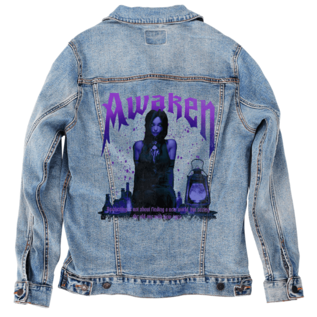 back view of a stonewashed denim jacket featuring a seated gothic figure surrounded by glowing potion bottles and a lantern. bold purple text above reads “Awaken,” with magical particles rising into the air. the artwork “Awaken” by DeRouche Designs is digitally printed on the jacket’s back panel by DenimINK.