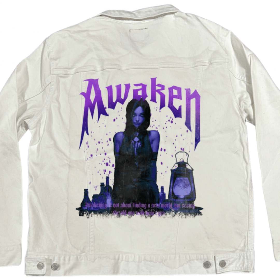 back view of a white denim jacket featuring a moody violet-toned illustration of a seated gothic figure surrounded by glowing potion bottles and a lantern. bold purple lettering across the top spells “Awaken.” the artwork “Awaken” by DeRouche Designs is digitally printed on the jacket’s back panel by DenimINK.