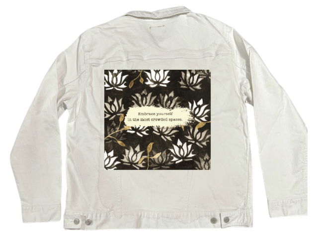 back view of a white denim jacket featuring the artwork “Be Yourself” by Canvas & Quotations, showing layered white lotus patterns, gold leaf accents, and the quote “Embrace yourself in the most crowded spaces” across a cream brushstroke. the artwork is digitally printed on the jacket’s back panel by DenimINK