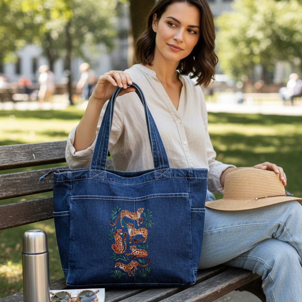 Woman holding a blue tote bag with floral design on a park bench. cheetah-collection-by-CatCoq-denim-tote-bag-lifestyle-shot