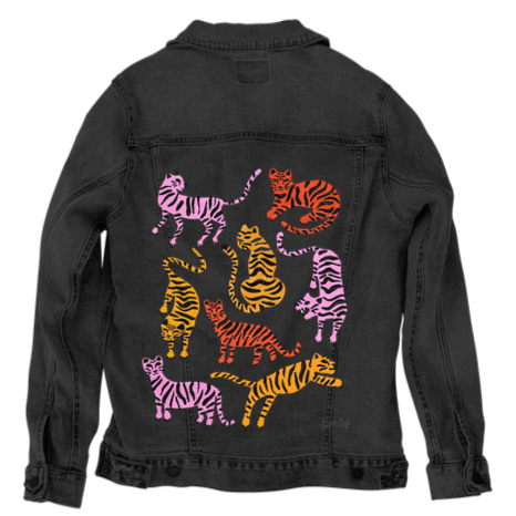 back view of a black denim jacket printed with the “Cheetah Collection” artwork by CatCoq, showing five cheetahs in active and resting poses, painted in warm orange tones with black spots. the cheetahs are surrounded by layered fern and palm leaves in varied green hues. the illustration is vertically centered and stands out vividly against the deep black fabric. printed by DenimINK on a unisex handcrafted jacket.