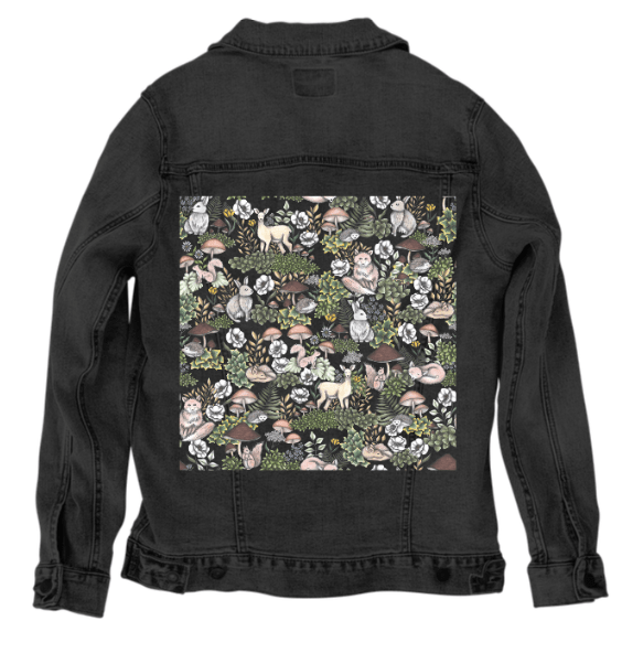 back view of a black denim jacket featuring the artwork “Into the Woods” by Cecilia Battaini, a repeating forest scene with sketched deer, sleeping foxes, mushrooms, ferns & wildflowers in soft creams, browns, moss green & slate. the rich black fabric deepens the contrast, making each animal & leaf appear like a glowing illustration on the forest floor. the design is digitally printed on the jacket’s back panel by DenimINK.