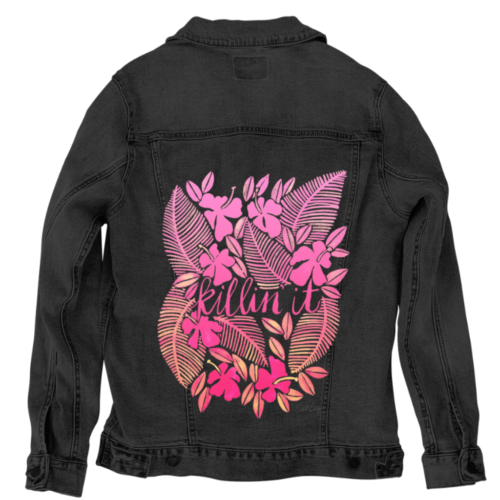 back view of a black denim jacket featuring the artwork “Killin' It” by CatCoq, digitally printed by DenimINK. the design includes the handwritten phrase “killin it” framed by overlapping tropical ferns & layered floral shapes in shades of coral, pink & blush. the bold colors pop vividly against the black denim, bringing vibrant contrast to the detailed botanical artwork.