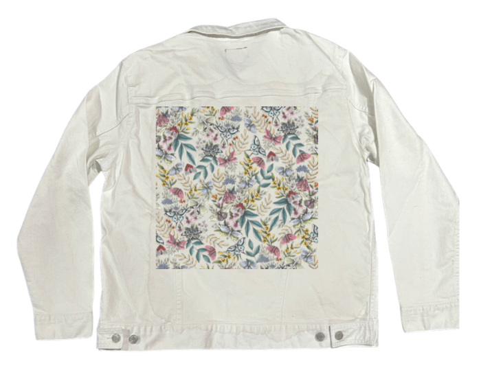 back view of a white denim jacket featuring the artwork “Midnight Garden” by Cecilia Battaini, showing moths with detailed wings weaving through wildflowers, leaves & berry-laden stems in muted tones of blush, mint, soft gold & plum. the white fabric allows the fine lines & natural palette of the illustration to shine through with delicate clarity. the design is digitally printed on the jacket’s back panel by DenimINK.