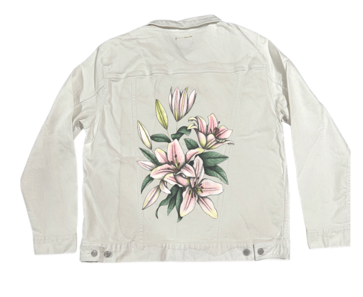 back view of a white denim jacket featuring a vertical floral artwork of soft pink lilies with subtle graphite texture & pale yellow-green leaf buds. the composition has a clean, light feeling that pairs smoothly with the crisp white denim. the artwork “Pink Lilies” by Cecilia Battaini is digitally printed on the jacket’s back panel by DenimINK.