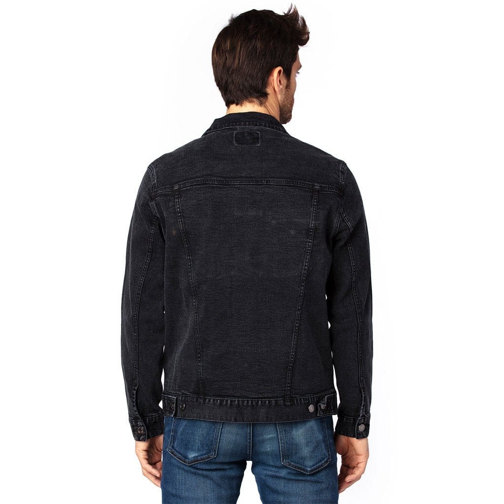 back view of a model standing in a studio wearing a black unisex retail-fit style classic-cut denim jacket showing stitching and clean print panel with no artwork