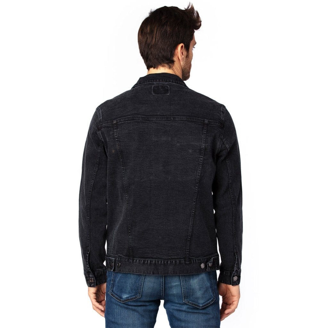 back view of a model standing in a studio wearing a black unisex retail-fit style classic-cut denim jacket showing stitching and clean print panel with no artwork