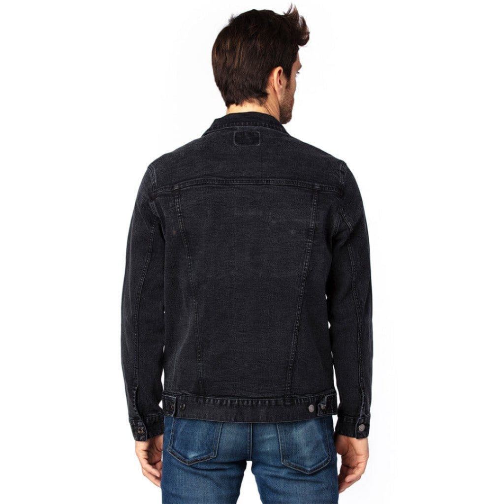 back view of a model standing in a studio wearing a black unisex retail-fit style classic-cut denim jacket showing stitching and clean print panel with no artwork