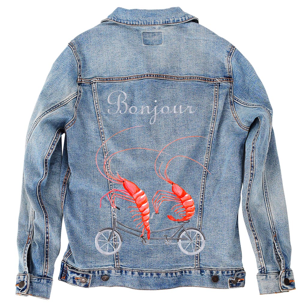 A denim jacket with a graphic design of shrimp riding a bicycle on the back, featuring the text 'Bonjour' and a wheeled design.