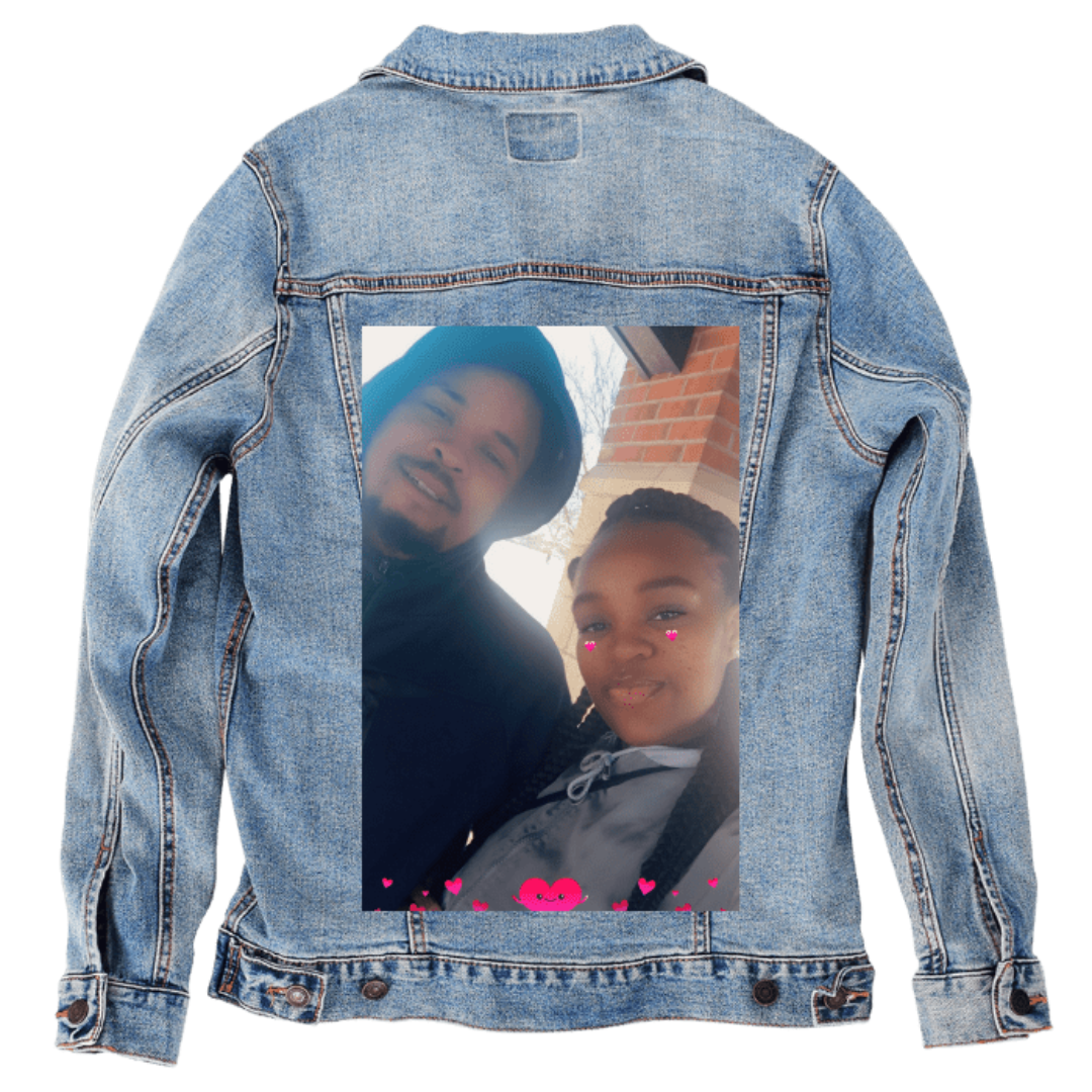 Customer designed custom denim jacket (M stonewash) featuring an outdoor selfie of two people printed on the back. The pair stands beneath a brick overhang, bundled in hooded and layered clothing as bright daylight washes across their faces. Soft digital pink heart filters float near their cheeks and along the bottom edge of the photo, adding a playful, affectionate tone. Subtle shadows, winter light, and the textured denim background create a warm, candid moment printed on denim jacket by DenimINK.