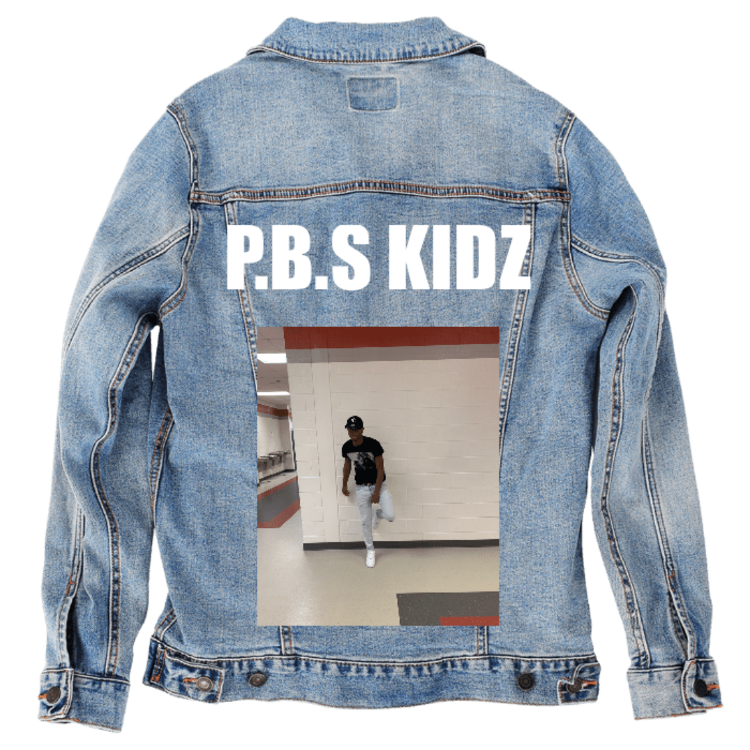 Customer designed custom denim jacket (S stonewash) featuring bold white lettering across the upper back that reads “P.B.S KIDZ,” paired with a full-color portrait photo below. The image shows a person posing in a school-like hallway with white block walls, red trim, and tiled flooring, wearing casual clothing and leaning with one leg lifted. The personalized text and candid photo create a lively custom design against the faded blue denim, printed on denim jacket by DenimINK.