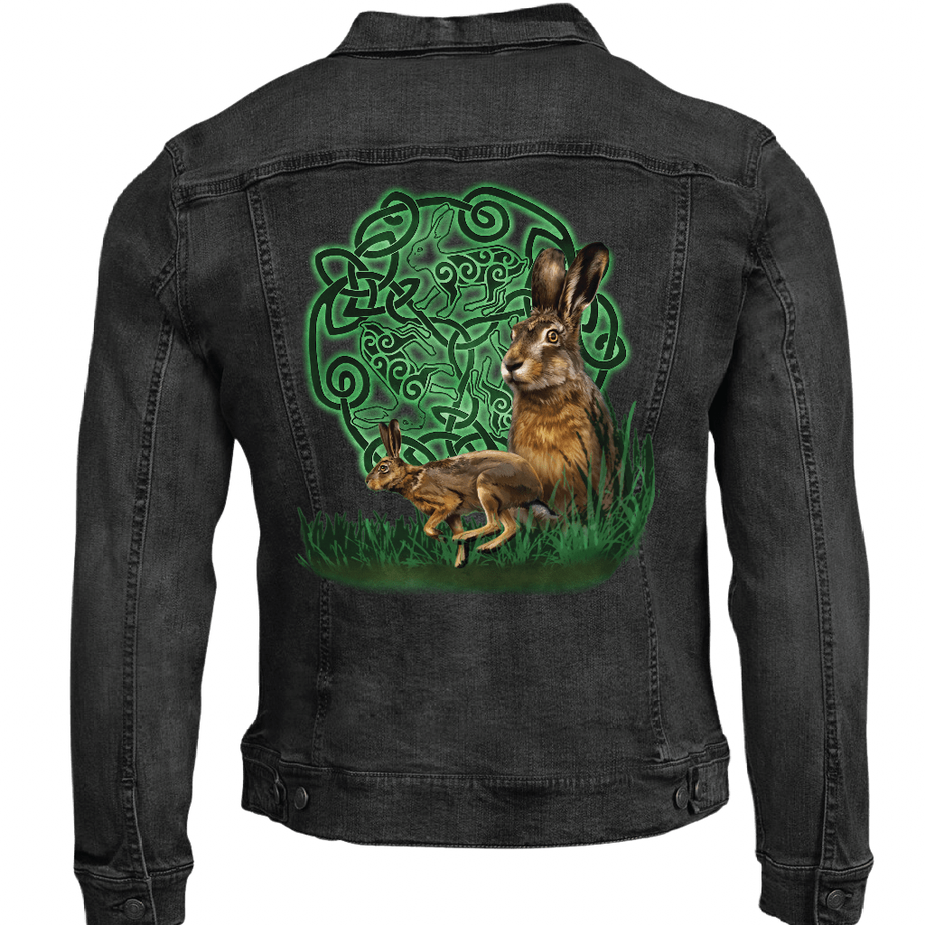 back view of a black denim jacket featuring the artwork “celtic hare” by brigid ashwood, printed centered on the back panel. the artwork shows two brown hares, one standing alert and one crouched, positioned in green grass in front of a glowing green celtic knotwork circle with animal motifs woven into the design, standing out clearly against the dark denim. digitally printed by DenimINK.