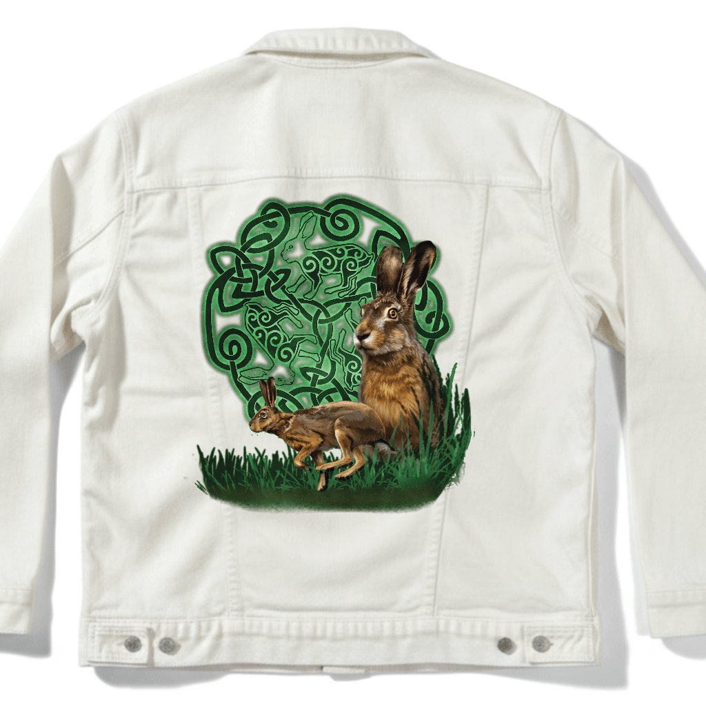 back view of a white denim jacket featuring the artwork “celtic hare” by brigid ashwood, printed centered on the back panel. the artwork shows two brown hares, one standing alert and one crouched, set in green grass in front of a glowing green celtic knotwork circle with animal motifs woven into the design, creating strong contrast against the white denim. digitally printed by DenimINK.