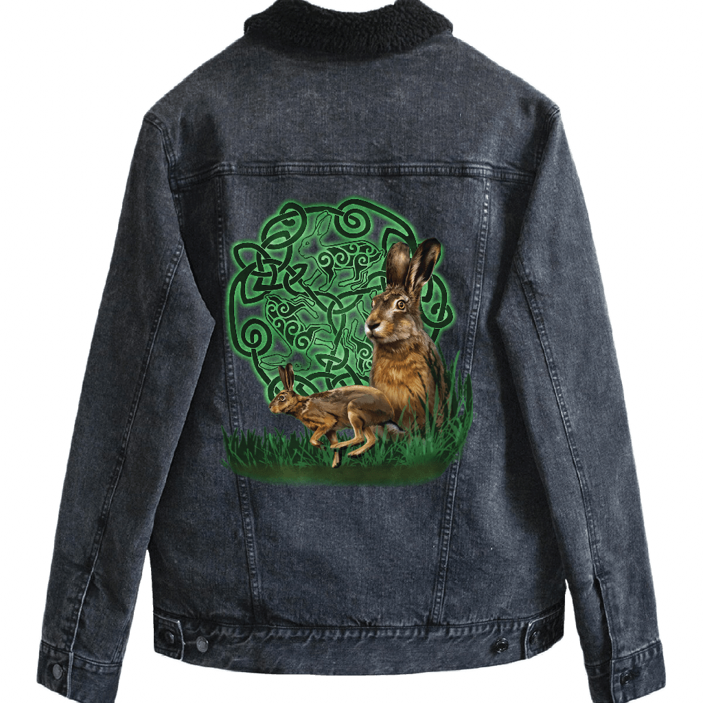 back view of a black denim jacket featuring the artwork “celtic hare” by brigid ashwood, printed centered on the back panel. the artwork shows two brown hares, one standing alert and one crouched, set in green grass in front of a glowing green celtic knotwork circle with animal motifs woven into the design, standing out clearly against the dark denim. the jacket includes a black sherpa-style liner visible at the collar. digitally printed by DenimINK.