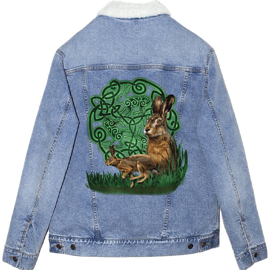 back view of a stonewash blue denim jacket featuring the artwork “celtic hare” by brigid ashwood, printed centered on the back panel. the artwork shows two brown hares, one standing alert and one crouched, set in green grass in front of a glowing green celtic knotwork circle with animal motifs woven into the design. the jacket includes an off-white sherpa-style liner visible at the collar. digitally printed by DenimINK.