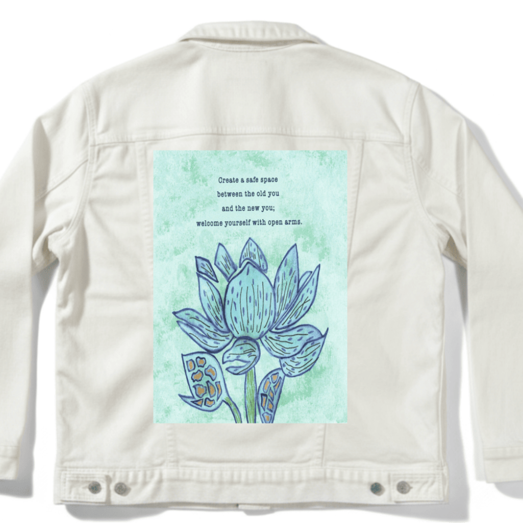 white denim jacket mockup featuring a blue lotus flower on a textured light-green background, paired with the quote “Create a safe space between the old you and the new you; welcome yourself with open arms.” the artwork is titled “Always Welcome Yourself” and created by Canvas &amp; Quotations (Monika Chugh and Alka Chopra) and printed by DenimINK