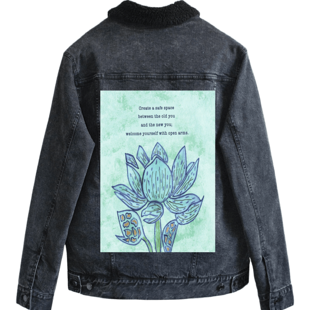sherp-lined black denim jacket mockup featuring a blue lotus flower on a textured light-green background, paired with the quote “Create a safe space between the old you and the new you; welcome yourself with open arms.” the artwork is titled “Always Welcome Yourself” and created by Canvas &amp; Quotations (Monika Chugh and Alka Chopra) and printed by DenimINK