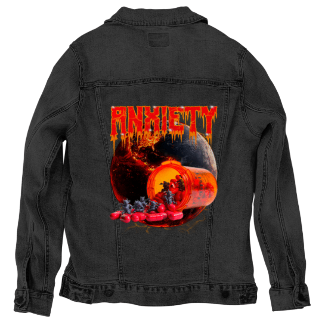 Flat lay of the back of a black denim jacket featuring the “Anxiety” design by DeRouche Designs. The back panel artwork is a chaotic scene of red pills releasing horned mini-demons, with a fiery cracked planet in the background. The black denim makes the fiery reds and oranges in the print glow intensely, amplifying the apocalyptic tone of the piece. Ideal for dark streetwear collections with a graphic edge. Printed by DenimINK