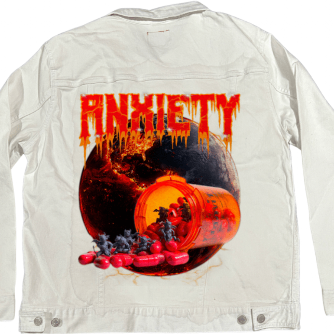 Flat lay of the back of a white denim jacket displaying the “Anxiety” artwork by DeRouche Designs on the back panel. The bright canvas allows the full-color spectrum of the design to stand out — from the translucent orange pill bottle to the molten planet and the demonic figures pouring from the capsules. A clean, eye-catching contrast between clinical whiteness and chaotic imagery. Printed by DenimINK