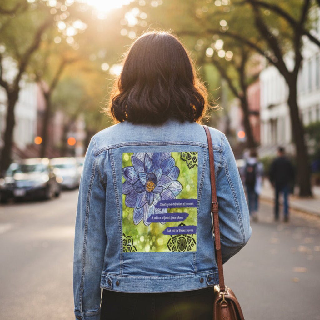 person wearing stonewashed denim jacket outdoors featuring a blue and purple lotus flower on a textured green background, paired with the quote “Create your definition of normal; it will be different from others but will be forever yours.” decorative black mandala-style motifs appear in the corners. this artwork is titled “Be Your Normal Self” and created by Canvas &amp; Quotations (Monika Chugh and Alka Chopra), printed by DenimINK