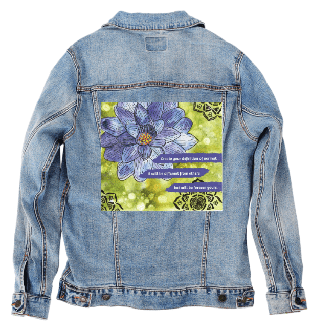 back view of a stonewash denim jacket showcasing the artwork “Be Your Normal Self” by Canvas &amp; Quotations, featuring a blue lotus flower, green watercolor-style background, and the quote “Create your definition of normal; it will be different from others but will be forever yours.” the artwork is digitally printed on the jacket’s back panel by DenimINK