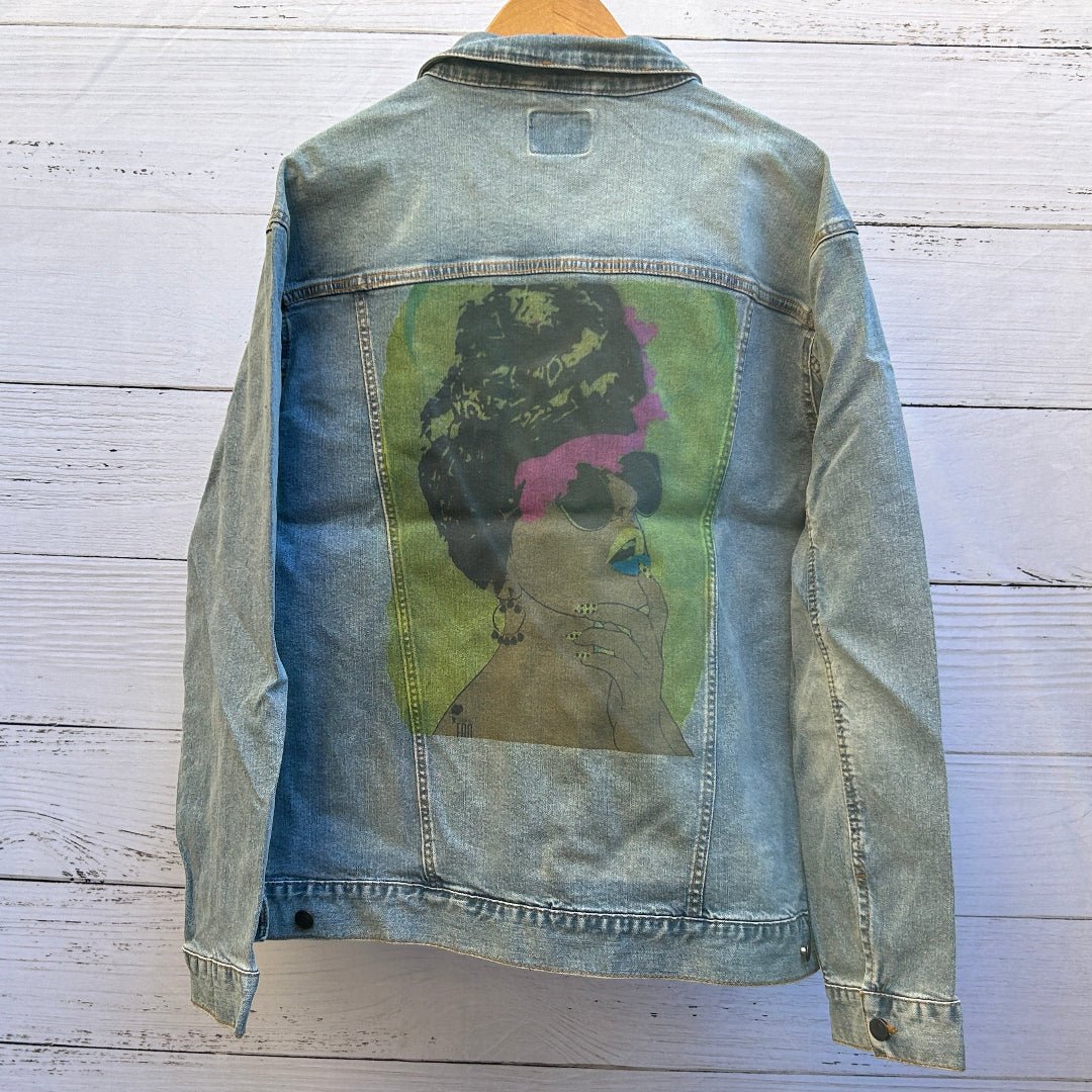Printed Denim Jacket. 3XL / Stonewashed. custom denim jacket showing a stylized side-profile portrait of a woman printed in muted earthy tones, featuring textured dark hair, a bold purple accent across the hairline, oversized dark sunglasses, blue lips, and a contemplative hand raised to her face, set against a soft green rectangular background; the print appears intentionally matte and slightly muted with visible denim grain and seams framing the artwo