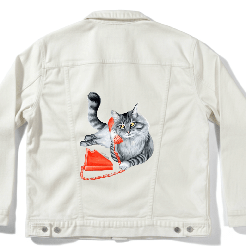 Mock up of a fluffy gray long-haired cat reclining with its tail curled upward, holding a bright red vintage telephone receiver to its ear Digitally printed by DenimINK on a unisex white denim jacket. the cat’s fur is rendered in layered charcoal and silver tones with fine whisker lines and golden-yellow eyes gazing forward. a matching red phone base and coiled cord rest below . titled “Cat on the Phone” and created by Amélie Legault 