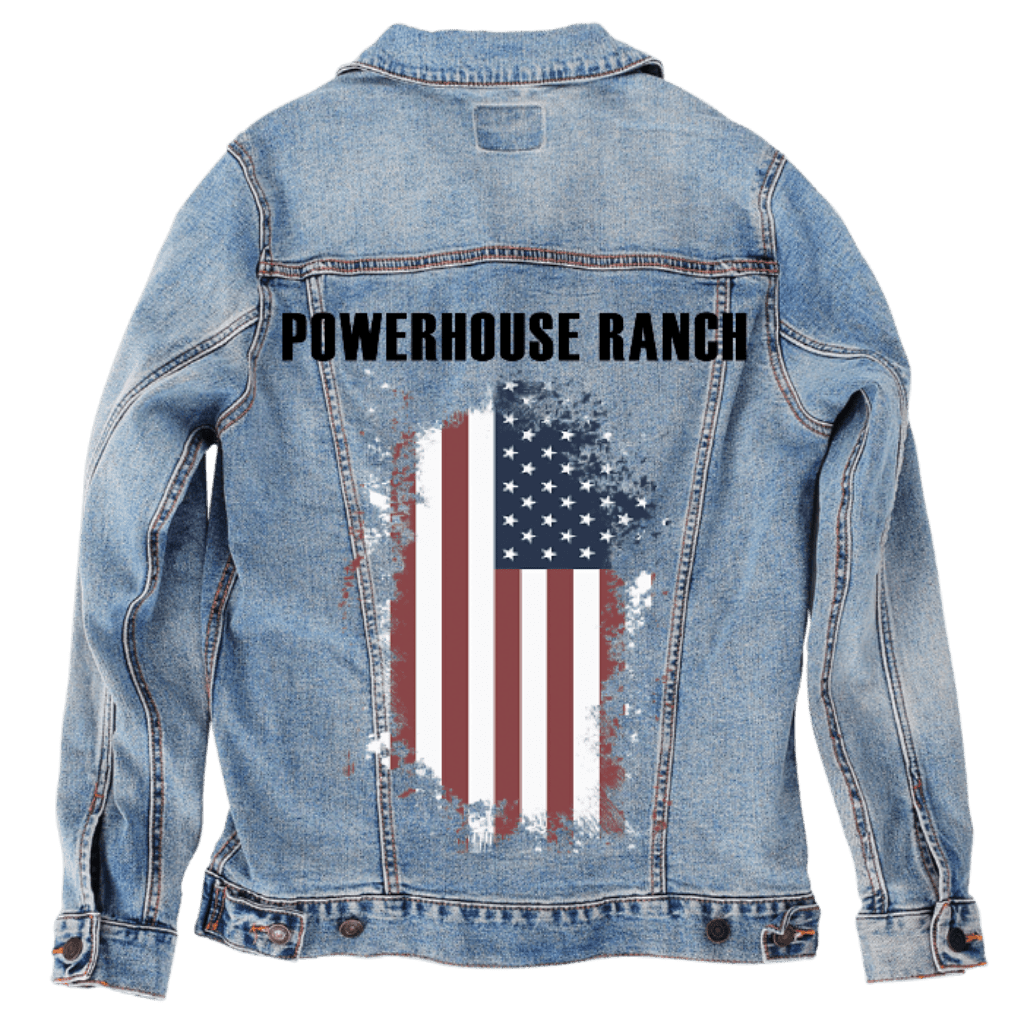 Back view of a stonewashed denim jacket displayed as a studio mockup, featuring bold black lettering reading “POWERHOUSE RANCH” across the upper back. A vertically oriented American flag appears below in a distressed, paint-worn style, with faded red stripes and weathered stars blending into the denim texture. The artwork feels rugged and intentional, like a working jacket made to represent land, pride, and perseverance. Printed by DenimINK