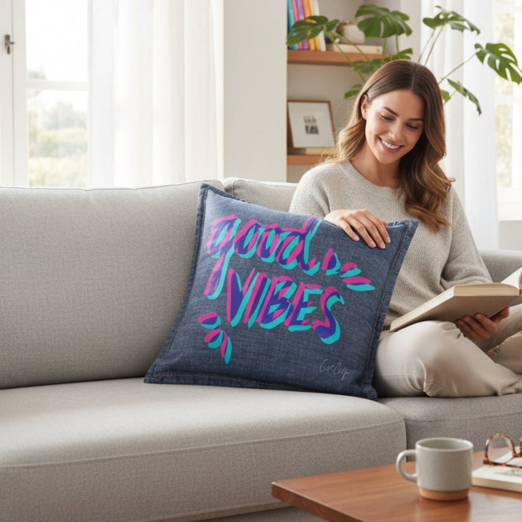 Woman reading a book on a couch with a 'Good Vibes' pillow.  good-vibes-by-catcoq-throw-pillow-lifestyle-shot