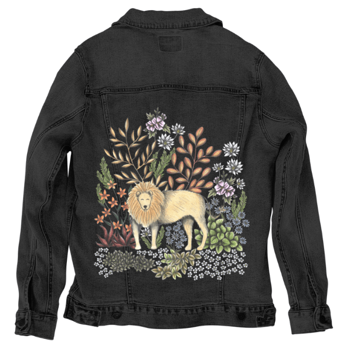 back view of a black denim jacket mockup featuring a digitally printed lion standing in a dense, moody botanical setting. the rich contrast between the black denim and the warm golds, rusts &amp; cool floral tones of the design amplifies the dreamy, enchanted forest mood. surrounded by succulents, star-like blossoms, &amp; pale glowing leaves, the lion appears calm &amp; regal. the artwork “Safari Lion” by Cecilia Battaini is digitally printed on the jacket’s back panel by DenimINK.