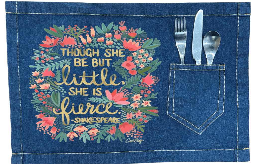 Denim placemat with floral design and Shakespeare quote, featuring a pocket for cutlery. with Shakespears quote "Though She Be But Little, She is Fierce" printed by DenimINK.   Little and Fierce by CatCoq on a denim table placemat mockup.