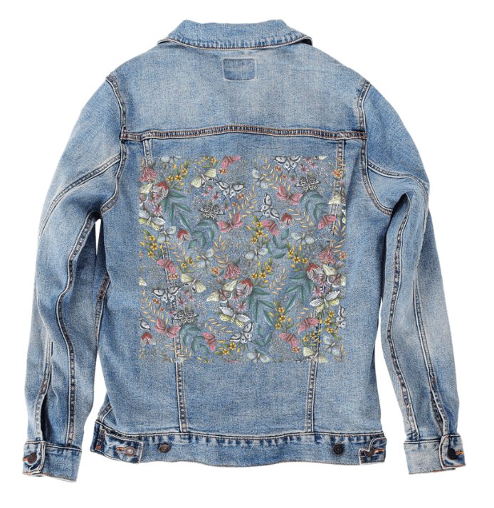 back view of a stonewashed denim jacket featuring the artwork “Midnight Garden” by Cecilia Battaini, a rich botanical repeat showing softly illustrated moths, ferns, wildflowers &amp; vines arranged like a moonlit thicket. the faded texture of the denim lends a soft, dreamlike atmosphere that blends beautifully with the pale sage, lavender &amp; cream tones. the design is digitally printed on the jacket’s back panel by DenimINK.
