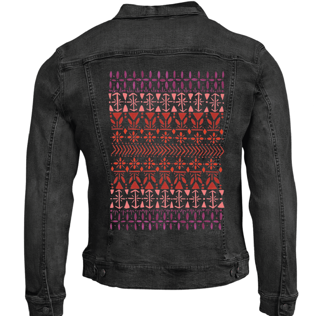 Black denim jacket with a vertically aligned Scandinavian folk pattern "Norwegian Pattern" by CatCoq made of repeating geometric rows including tulip shapes, arrows, diamonds, snowflakes &amp; stylized trees. the hand-painted elements fade from deep violet at the top to coral &amp; rust red toward the center, then shift to pink &amp; purple again. printed by DenimINK. mockup