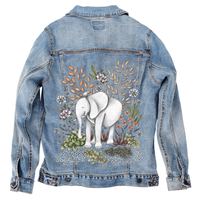 back view of a stonewashed denim jacket featuring a softly sketched white elephant surrounded by textured floral elements, including peach-toned grasses, green succulents, star-like wildflowers &amp; leafy botanicals in warm, vintage colors. the artwork “Safari Elephant” by Cecilia Battaini is digitally printed on the jacket’s back panel by DenimINK.