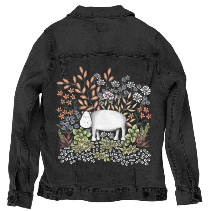 back view of a black denim jacket featuring an illustrated white hippo surrounded by detailed desert botanicals—golden stalks, dusky pink leaves, soft succulents, &amp; blue-gray blossoms. the artwork “Safari Hippo” by Cecilia Battaini is digitally printed on the jacket’s back panel by DenimINK.