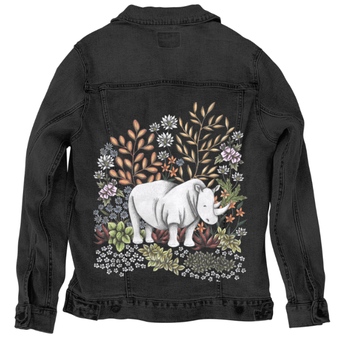back view of a black denim jacket mockup showcasing a digitally printed illustration of a white rhino in a lush desert bloom of warm ochre, charcoal succulents, purple daisies, and burnt orange blossoms. the artwork “Safari Rhino” by Cecilia Battaini is digitally printed on the jacket’s back panel by DenimINK.