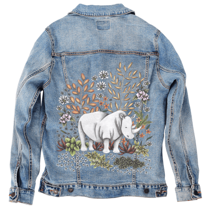back view of a stonewashed denim jacket markup  featuring a softly shaded white rhino standing among sage green succulents, dusty red aloe, pale blossoms, and warm-toned desert leaves. the artwork “Safari Rhino” by Cecilia Battaini is digitally printed on the jacket’s back panel by DenimINK.