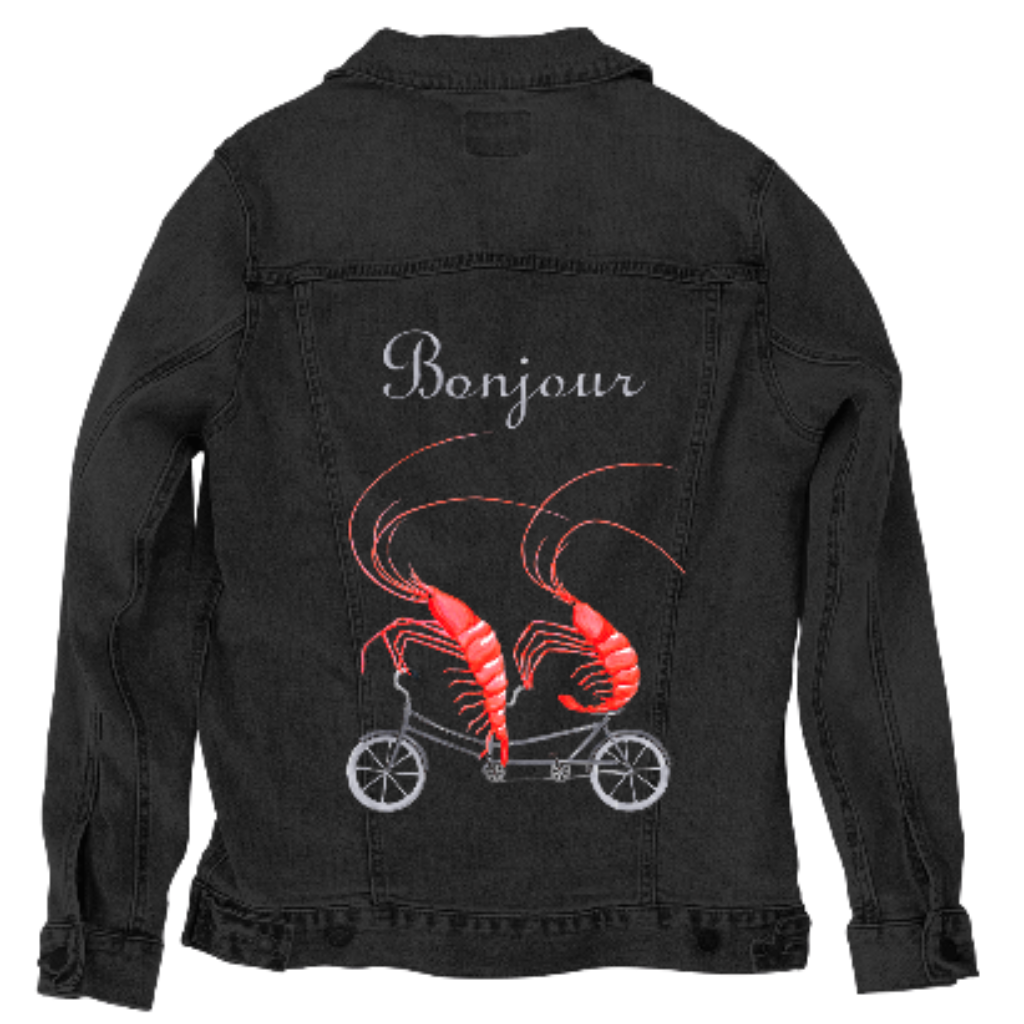 back view of a black denim jacket featuring the artwork “Shrimp Riding a Bicycle” by Amélie Legault, showing two bright red shrimp pedaling a small bicycle beneath the word “Bonjour.” the artwork is digitally printed on the jacket’s back panel by DenimINK