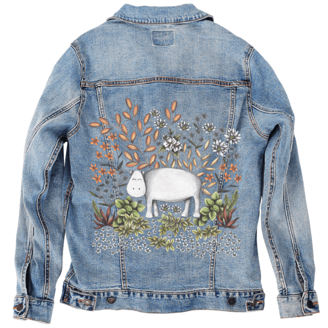 back view of a stonewashed denim jacket mockup featuring a cheerful white hippo in the center of an ornate garden illustration filled with pastel botanicals, warm clay-toned leaves, soft purples, ivory flowers &amp; desert greens. the artwork “Safari Hippo” by Cecilia Battaini is digitally printed on the jacket’s back panel by DenimINK.