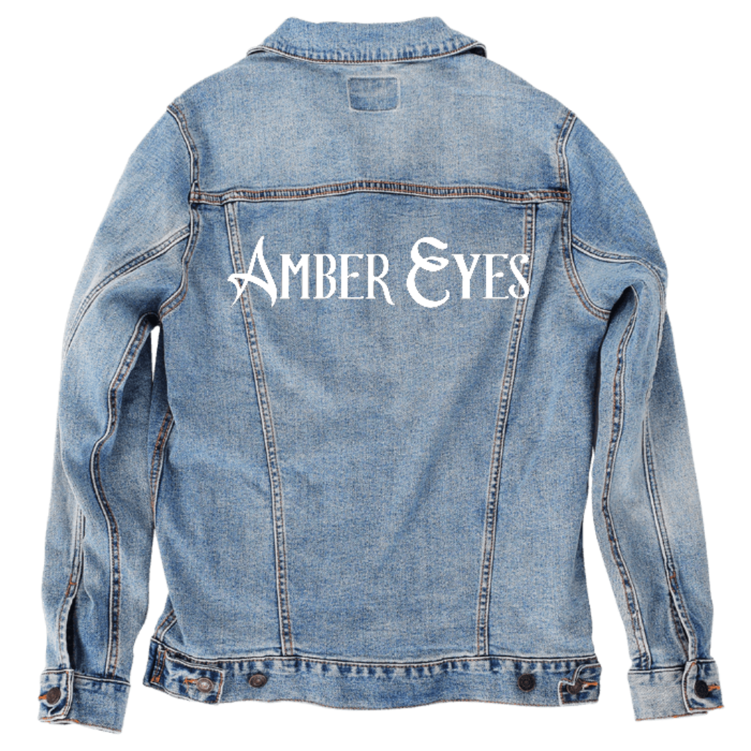 Customer designed custom denim jacket (S stonewash) featuring bold white gothic-style lettering across the upper back that reads “AMBER EYES.” The sharp, dramatic serifs and stylized letterforms create a striking medieval-inspired look that contrasts crisply with the soft, faded blue denim. The high-contrast typography gives the jacket a mysterious, expressive personality, printed on denim jacket by DenimINK.