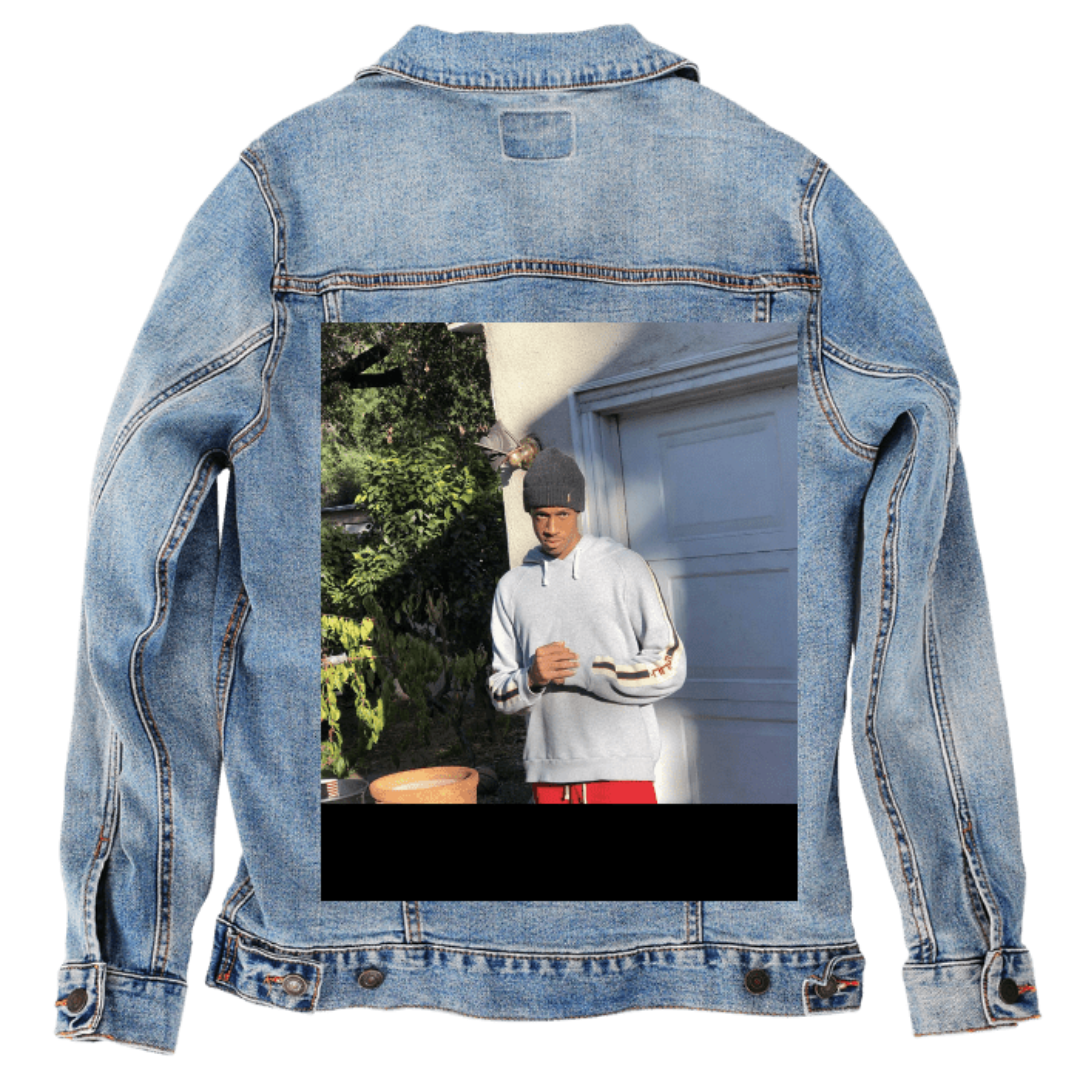 Customer designed custom denim jacket (S stonewash) featuring a full-color outdoor portrait printed on the back, showing a man in a light gray hoodie and dark beanie standing near a garage door with sunlit greenery behind him. The natural shadows and bright foliage give the scene a relaxed, candid feel that contrasts with the soft, faded blue denim, printed on denim jacket by DenimINK.