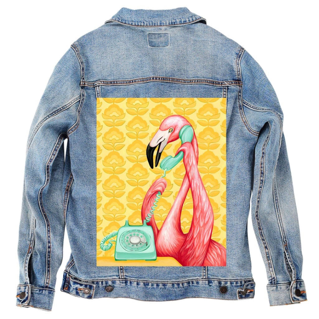 back view of a stonewash denim jacket featuring the artwork “Pink Flamingo on the Phone” by Amélie Legault, showing a pink flamingo holding a mint-green rotary telephone against a yellow patterned background. the artwork is digitally printed on the jacket’s back panel by DenimINK